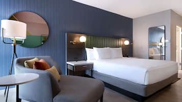 Quarto de hotel moderno com uma cama grande, um espelho redondo, uma escrivaninha e uma cadeira.