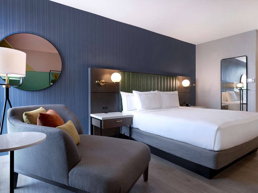 Quarto de hotel moderno com uma cama grande, um espelho redondo, uma escrivaninha e uma cadeira.