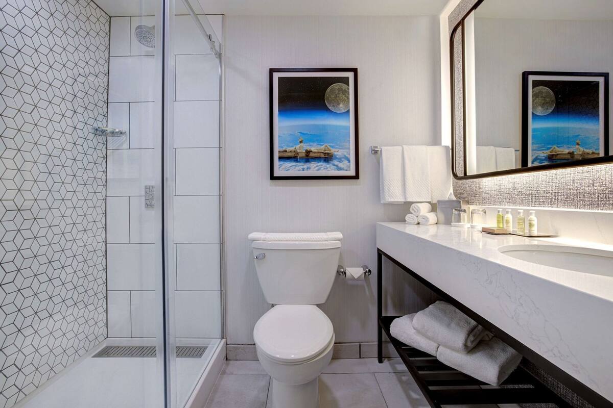 A modern bathroom with a glass shower enclosure, a toilet, a sink with a mirror, and two framed pictures on the wall.