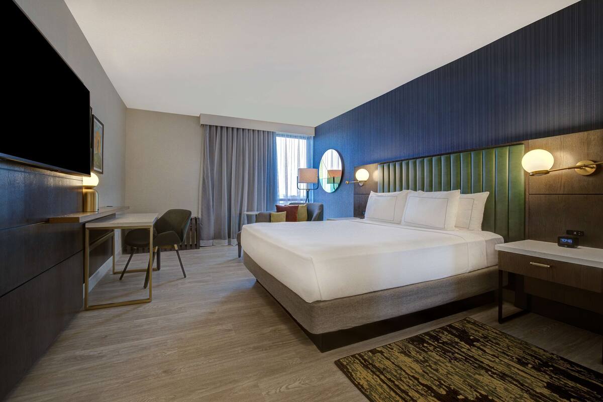 A modern hotel room with a large bed, a desk, and a television.