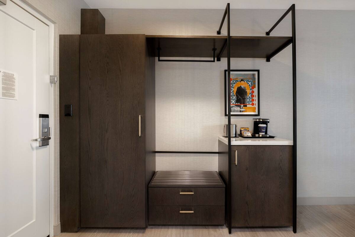 A modern room with a dark wood wardrobe, a small bench, and a coffee machine on a counter.