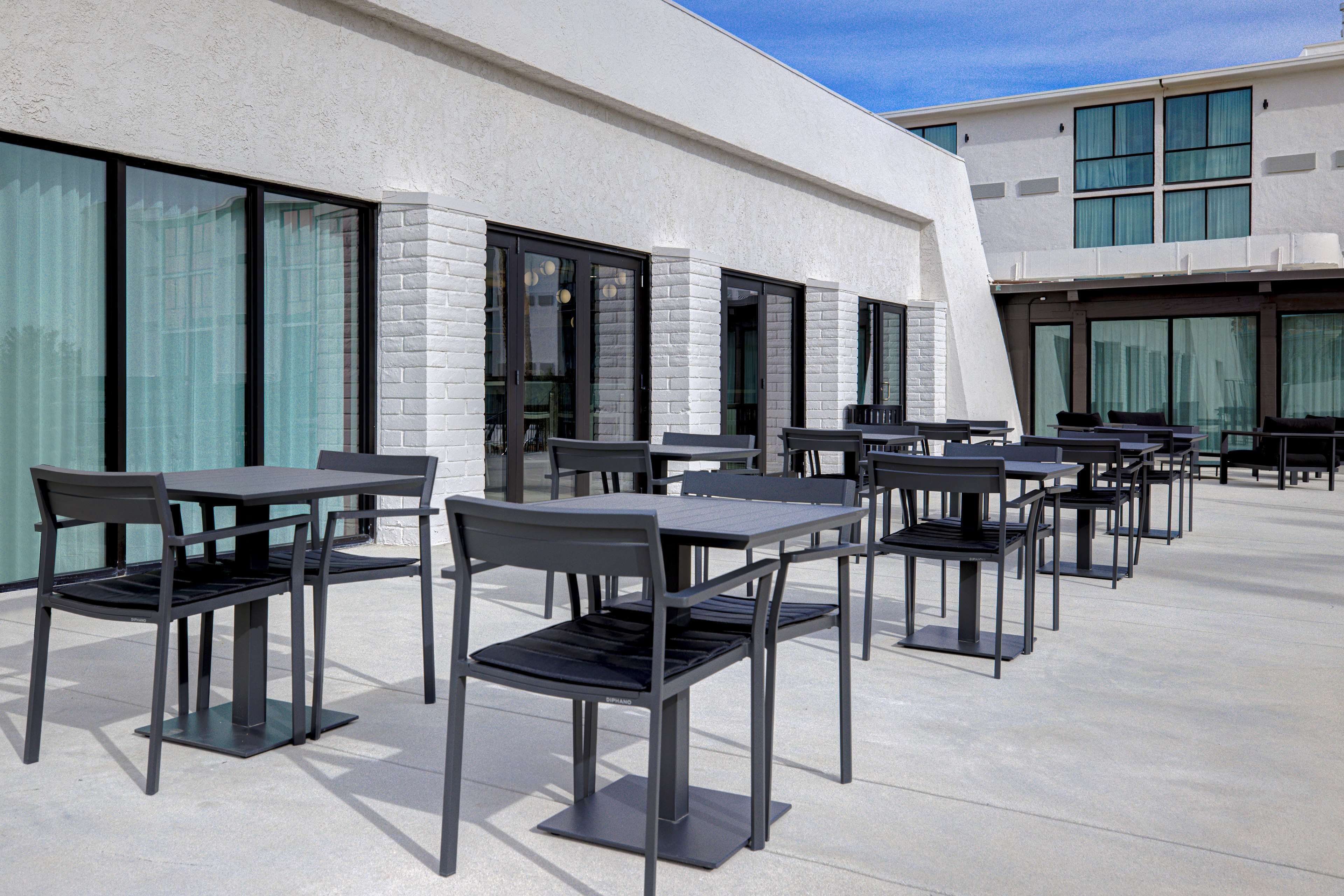 An outdoor seating area with multiple tables and chairs, a modern building facade, and large windows.