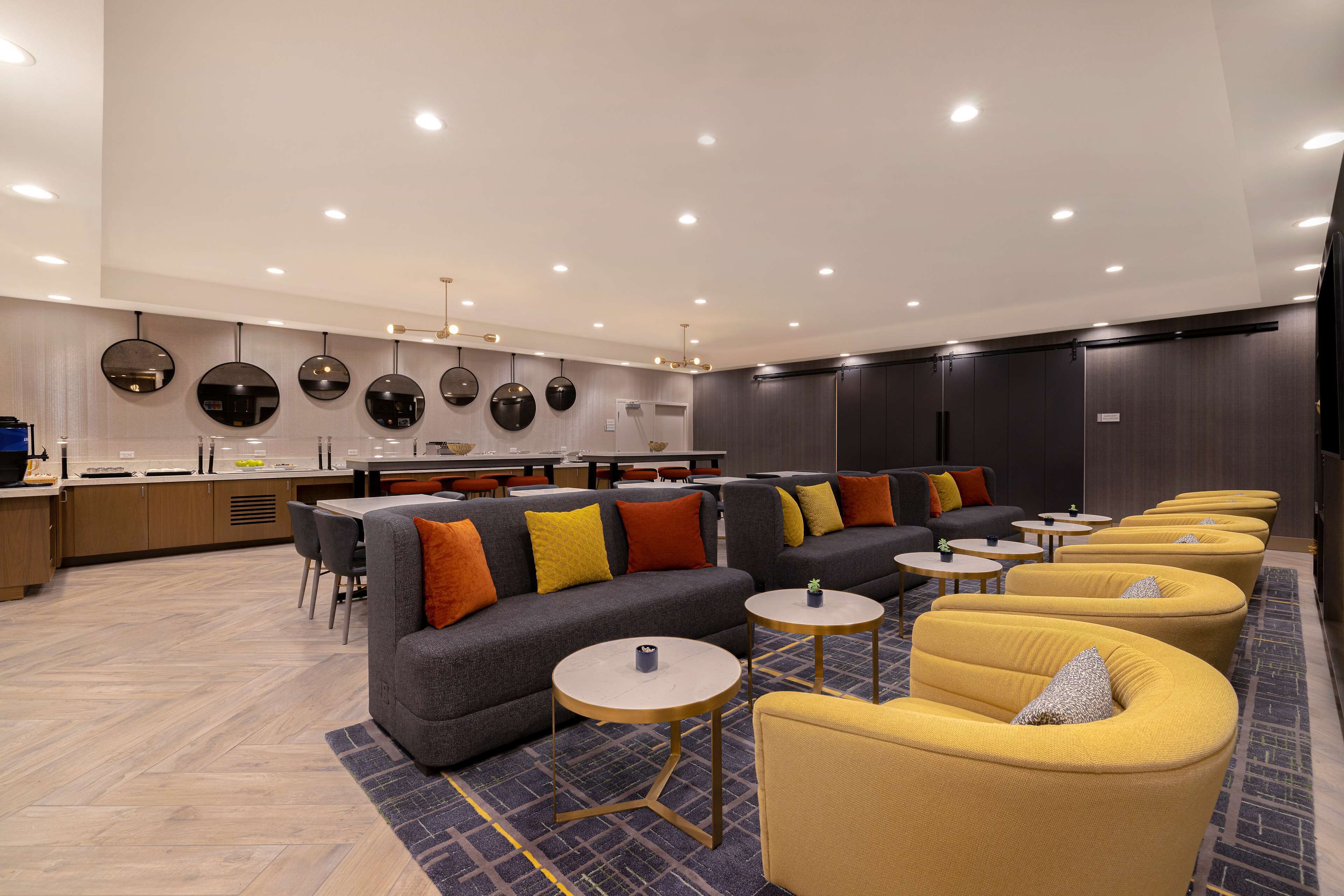 Een moderne zithoek met banken, fauteuils en kleine tafels, met op de achtergrond een keuken.