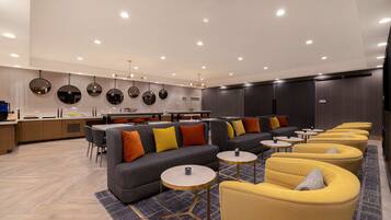 Een moderne zithoek met banken, fauteuils en kleine tafels, met op de achtergrond een keuken.