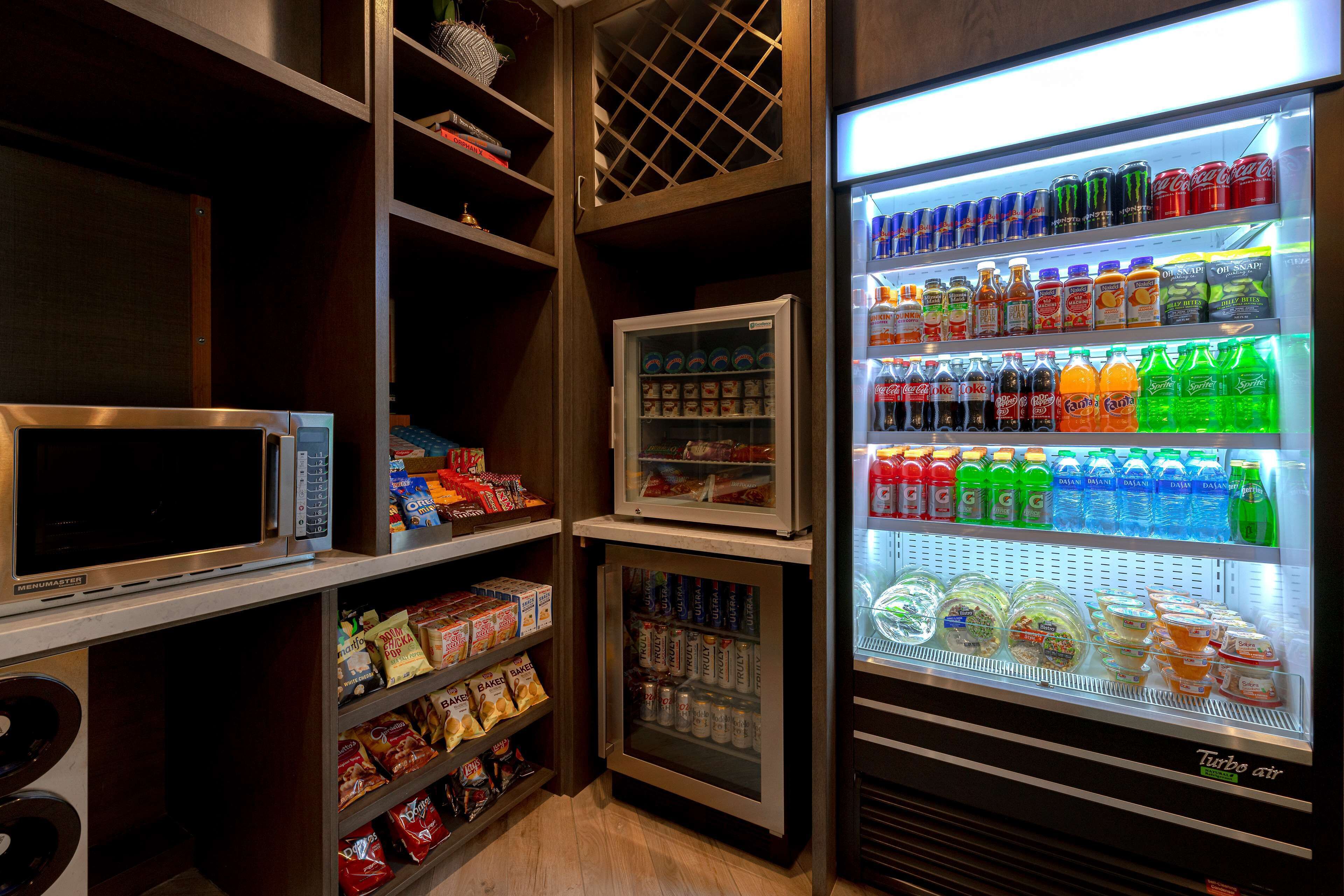 A vending machine stocked with various beverages and snacks, a microwave, and shelves with packaged food items.