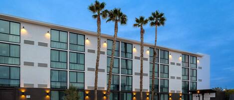 A modern hotel with a pool area, palm trees, and lounge chairs.