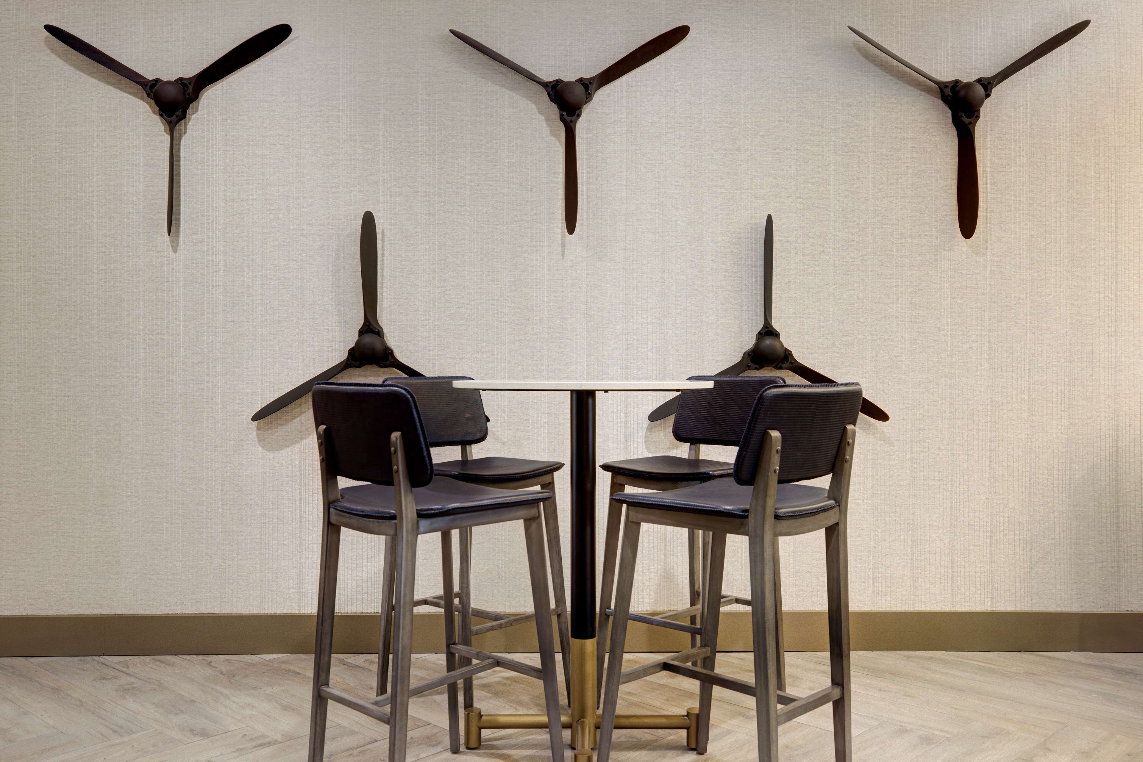 A dining area with a table and four chairs, three wall-mounted propeller-style light fixtures, and a light-colored textured wall.