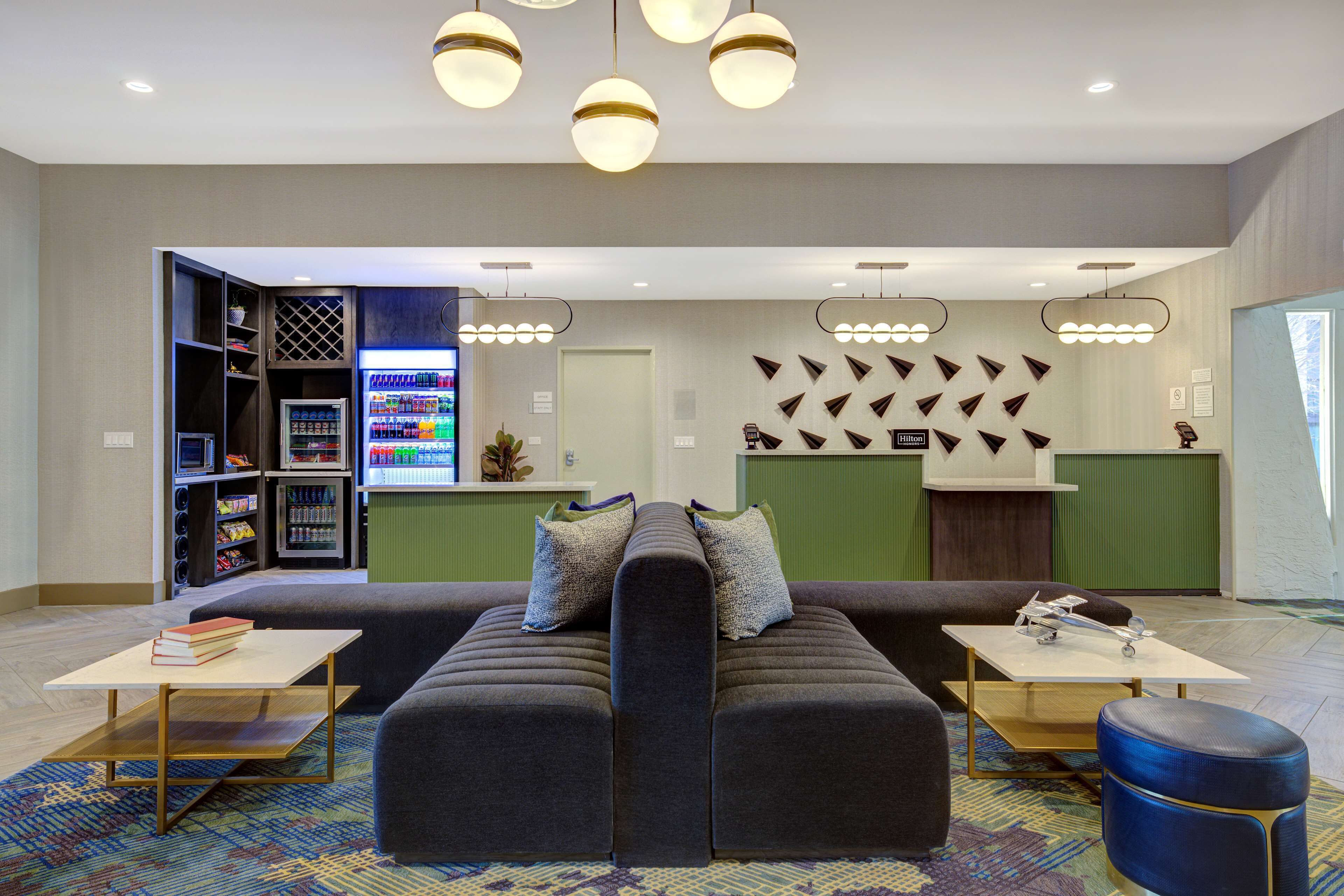 A modern lobby with a sofa, a reception desk, a vending machine, and a wall with a geometric pattern.