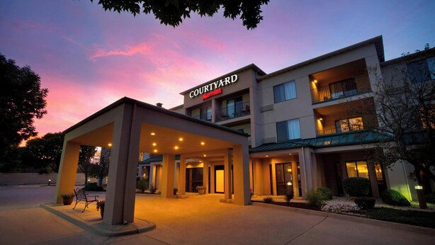 Un hotel Courtyard Marriott con entrada techada, varios pisos y jardín ajardinado en la parte delantera.
