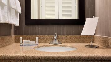 A bathroom with a granite countertop, a white sink, a mirror, and a towel rack.
