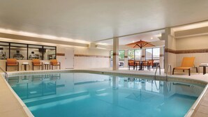 Una piscina con agua cristalina azul, rodeada de sillones de descanso y una mesa con sombrillas.