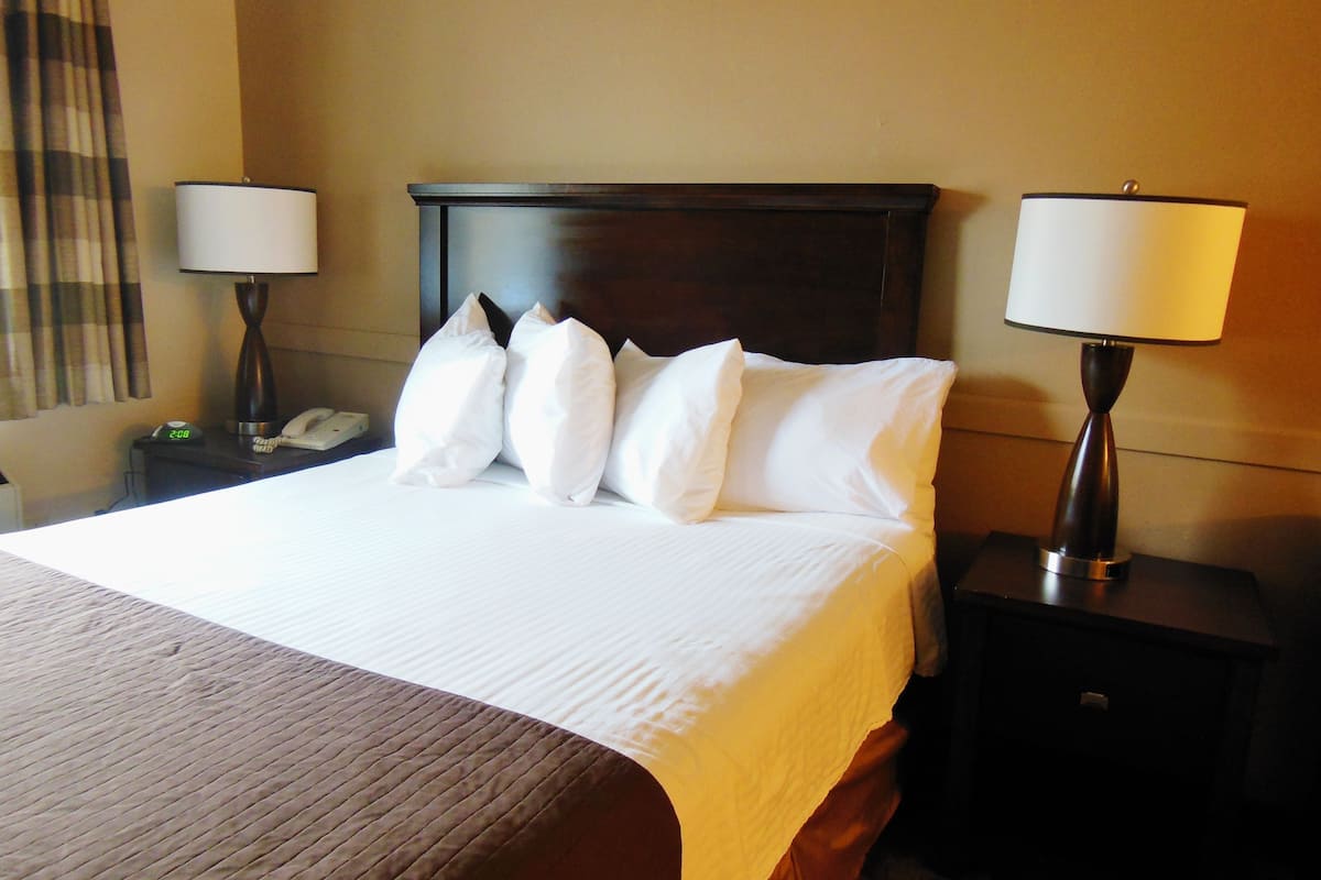 A neatly made bed with white linens and pillows, a wooden headboard, and two bedside lamps on nightstands.