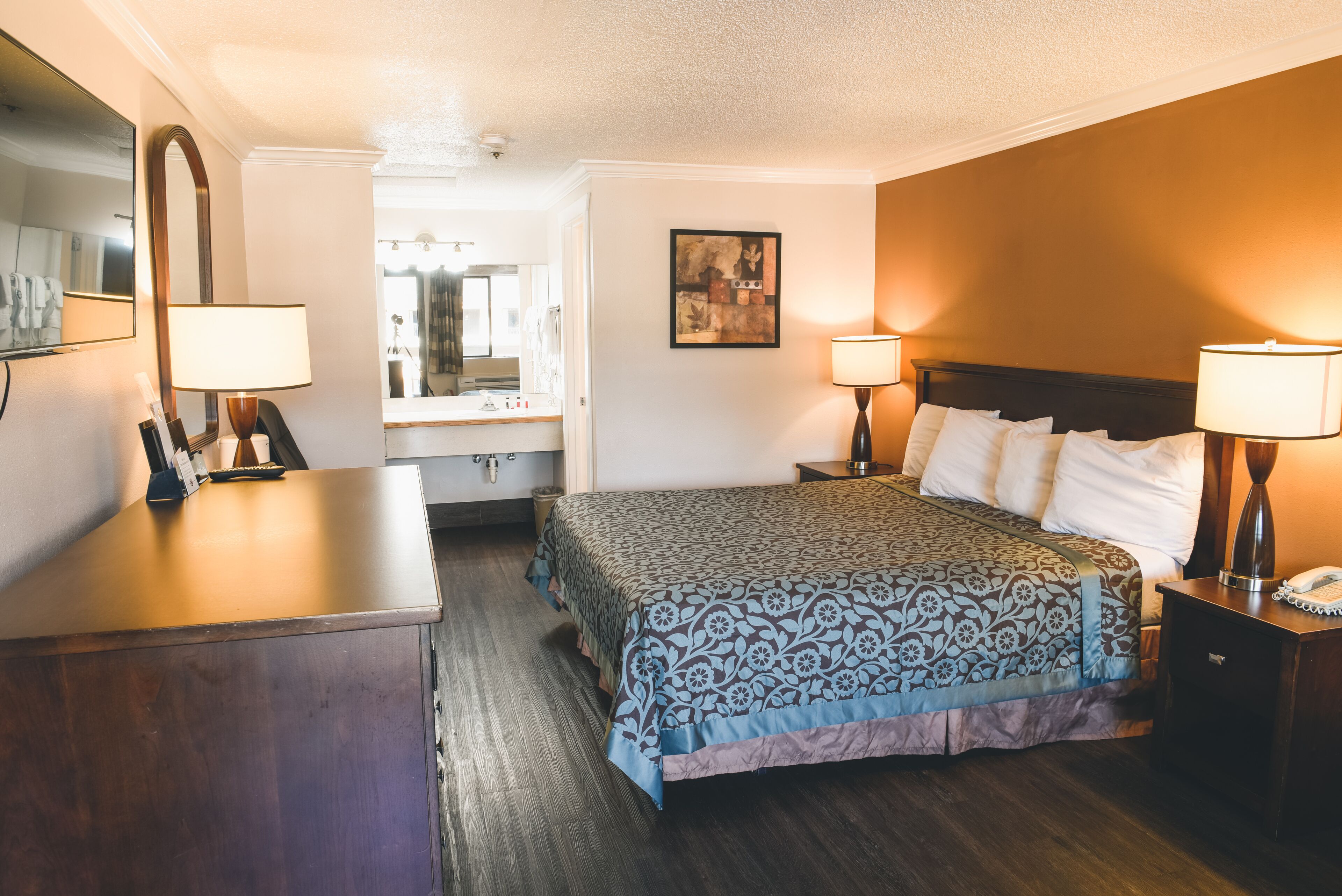 A hotel room with a large bed, bedside lamps, a desk with a lamp, a mirror, and a framed picture on the wall.