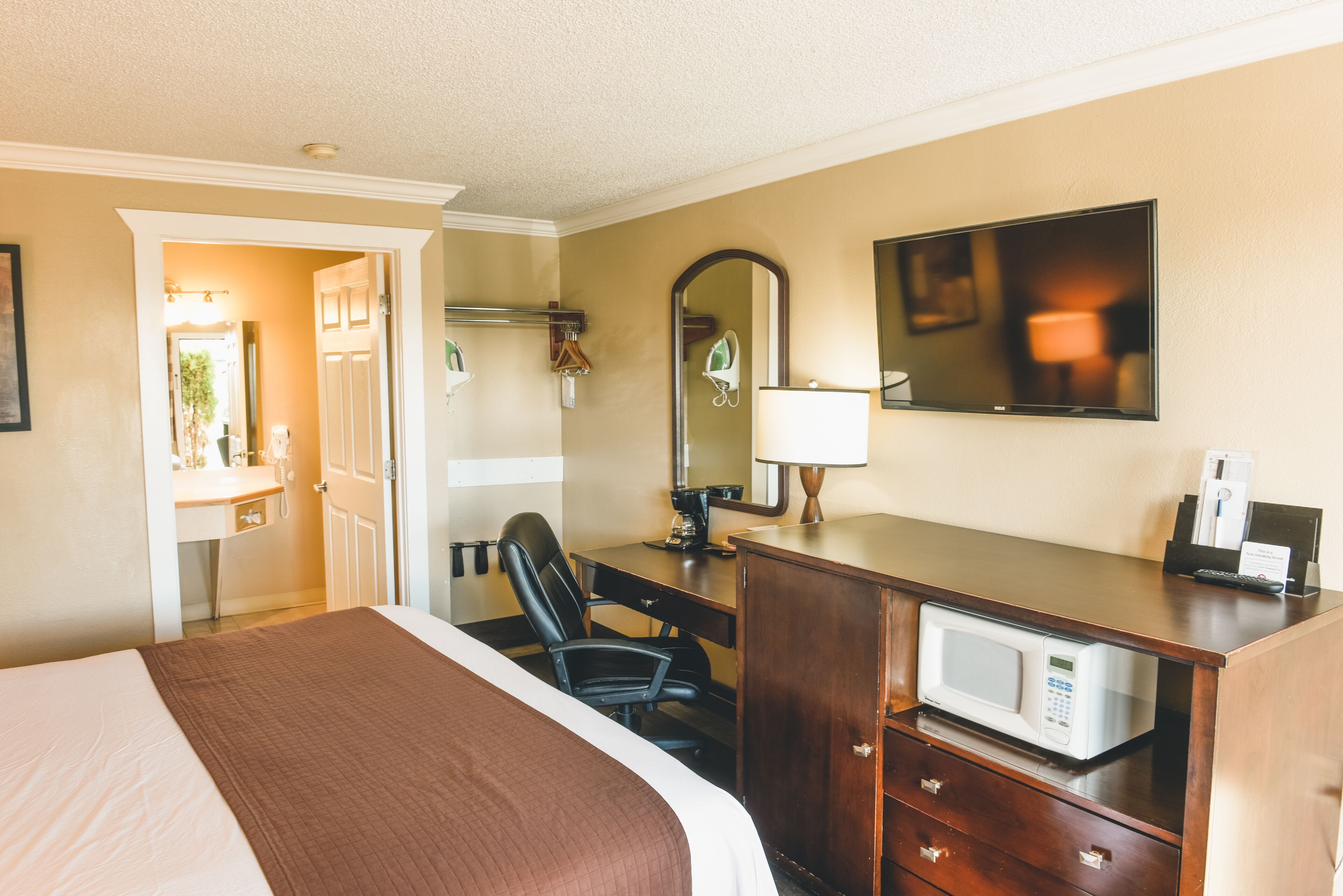 A hotel room with a bed, desk, chair, microwave, and a TV on the wall.