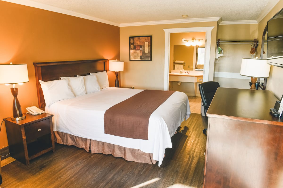 A hotel room with a large bed, bedside lamps, a desk, and a bathroom visible through an open door.