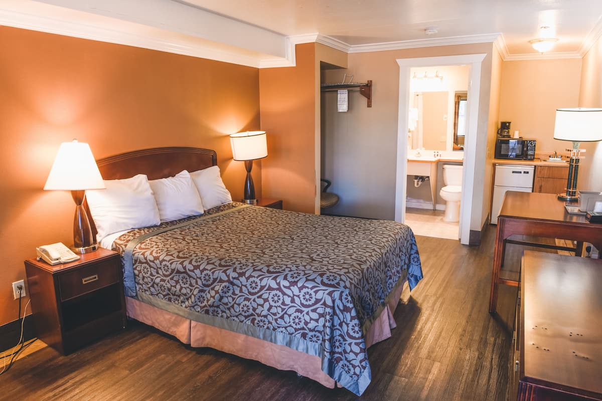 A hotel room with a large bed, bedside lamps, a desk, and a bathroom visible through an open door.