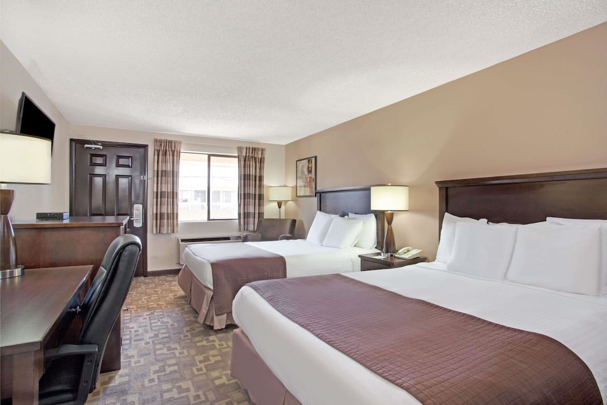 A hotel room with two beds, a desk, a chair, a telephone, and a window with curtains.