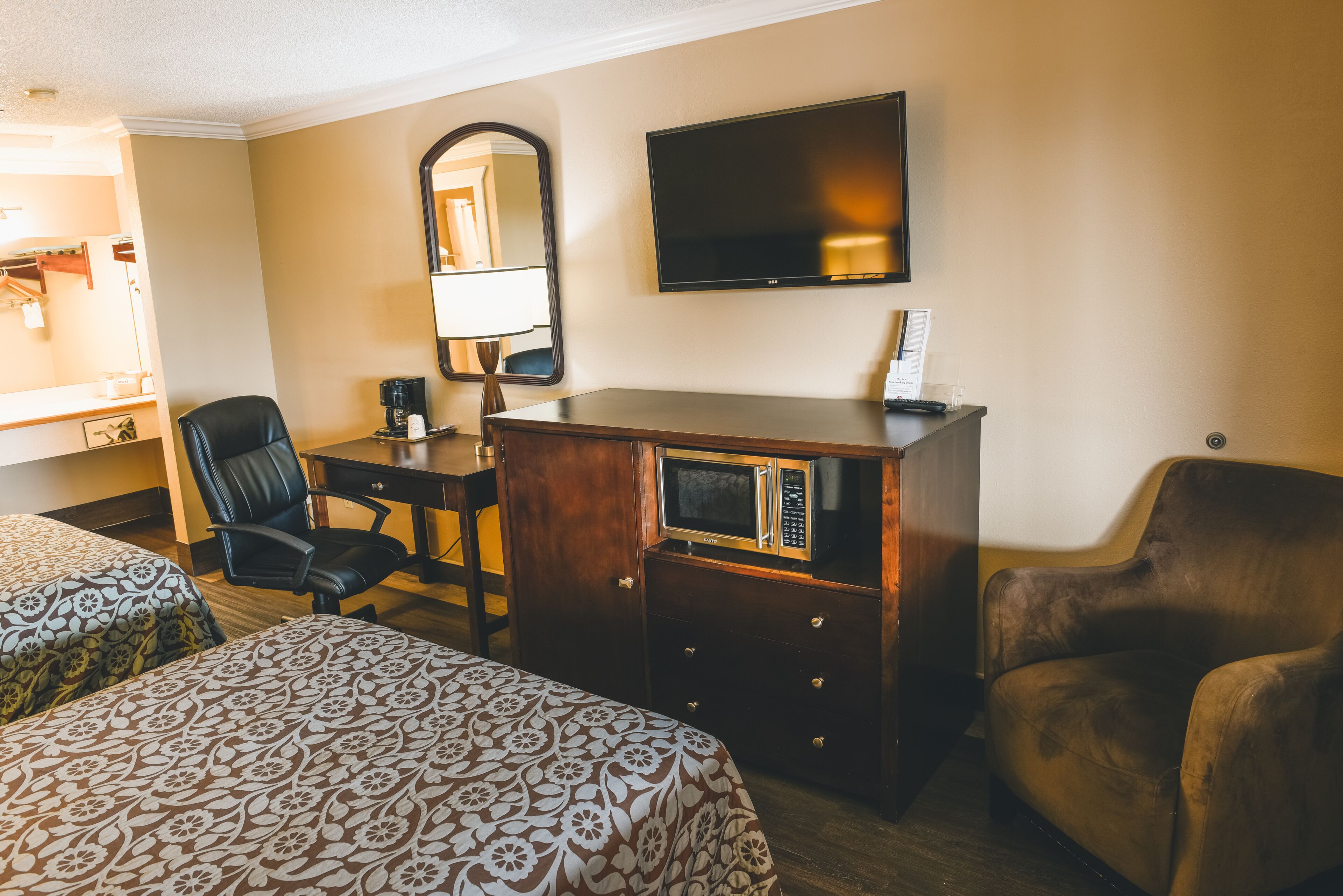 Ein Hotelzimmer mit zwei Betten, einem Schreibtisch mit Computer, einem Fernseher, einem Spiegel und einem Stuhl.