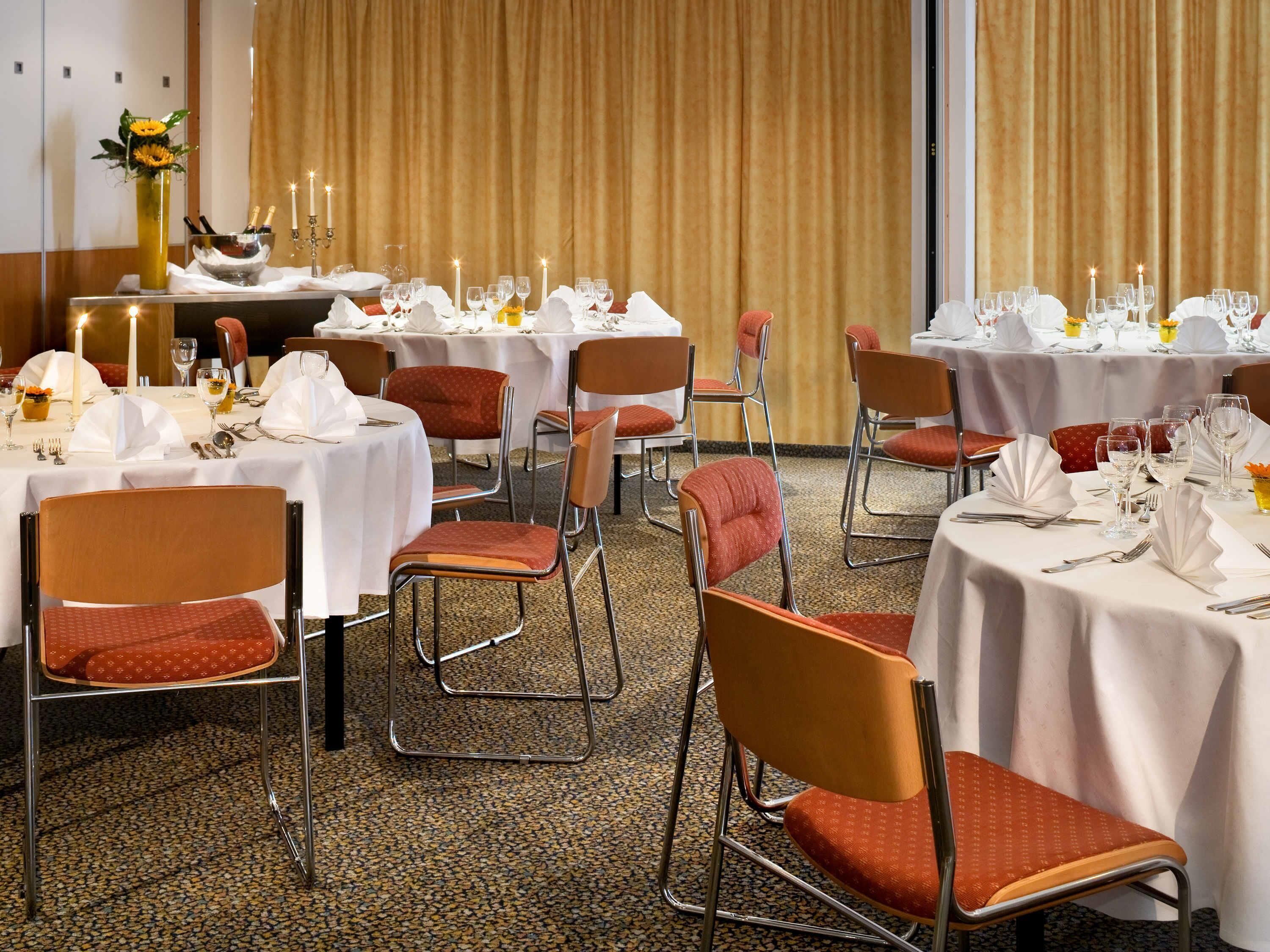 A banquet hall with round tables, chairs, and candle-lit centerpieces.