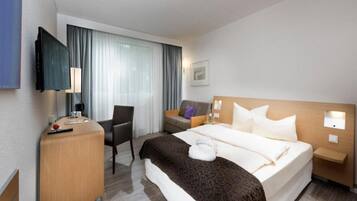 Una habitación de hotel con cama, escritorio, silla, televisor y ventana con cortinas.