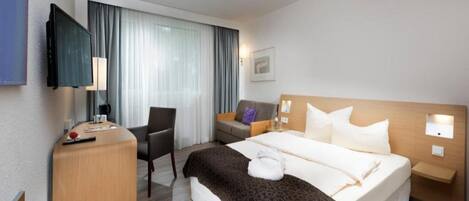 Una habitación de hotel con cama, escritorio, silla, televisor y ventana con cortinas.