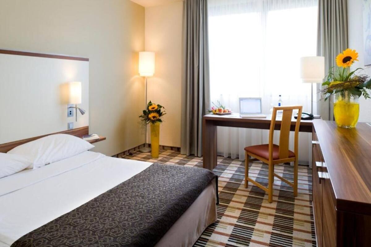 A hotel room with a bed, desk, chair, and a window with curtains.