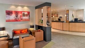 A hotel lobby with a reception desk, seating area with sofas and armchairs, a large abstract painting, and a reception counter. - Sunday Hotel Saarbrücken Süd (Saarbrücken)