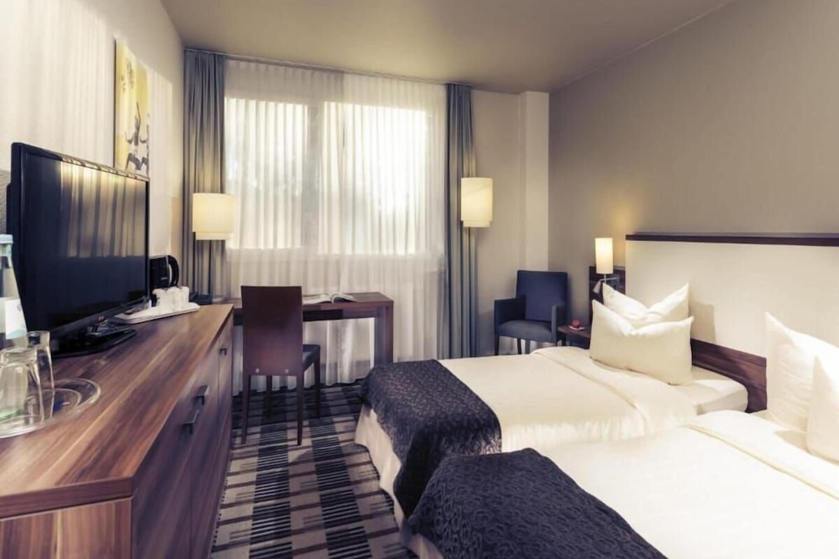 A hotel room with a bed, a desk, a chair, a television, and a lamp.