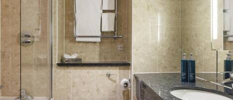 A bathroom with a glass-enclosed shower, a toilet, a sink with a mirror, and a towel rack with two towels.