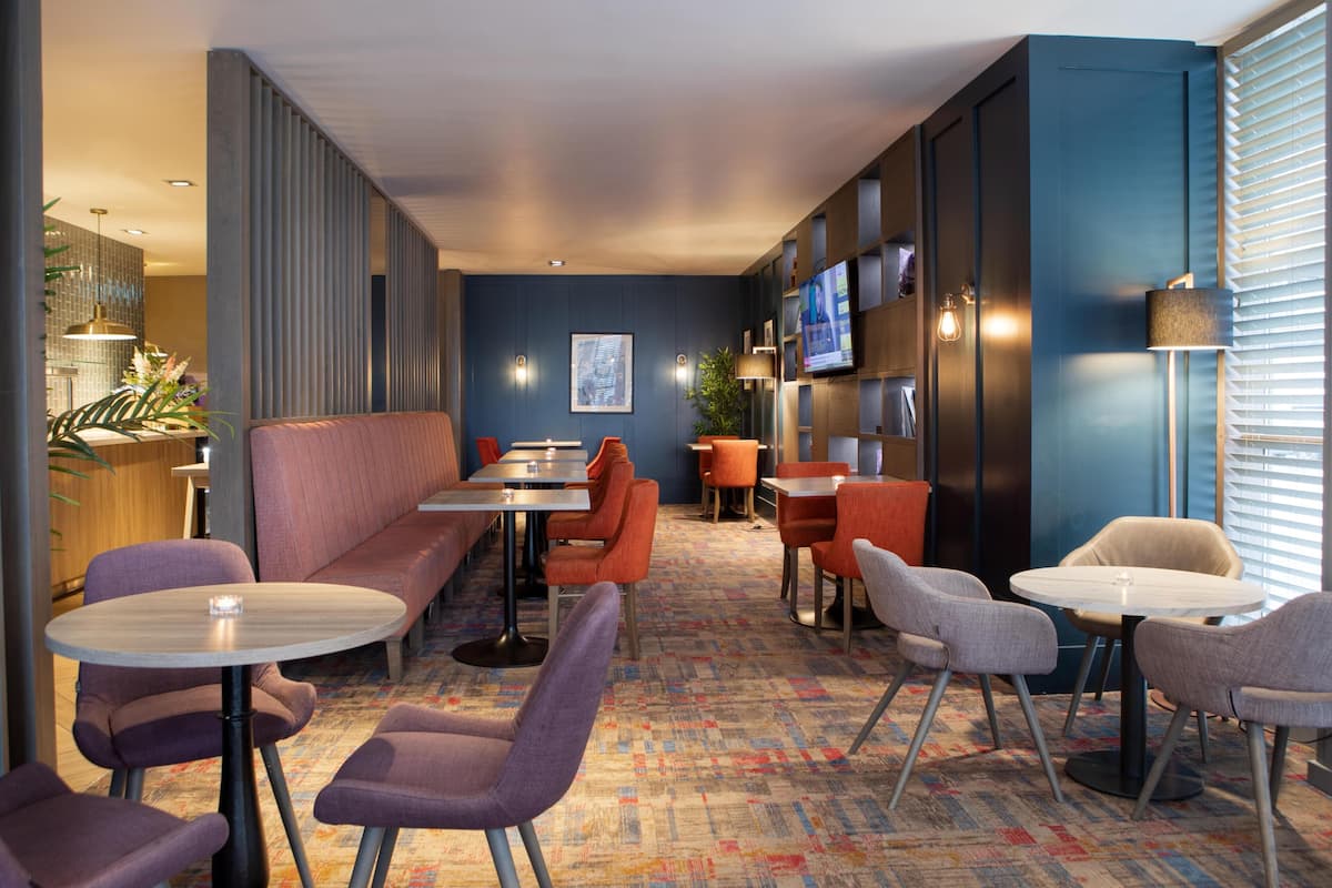 Een moderne hotel lobby met zithoeken, een bar en een televisiescherm.