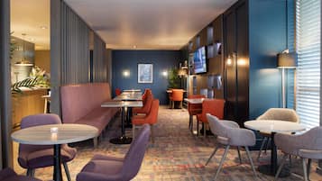 A modern hotel lobby with seating areas, a bar, and a television screen.