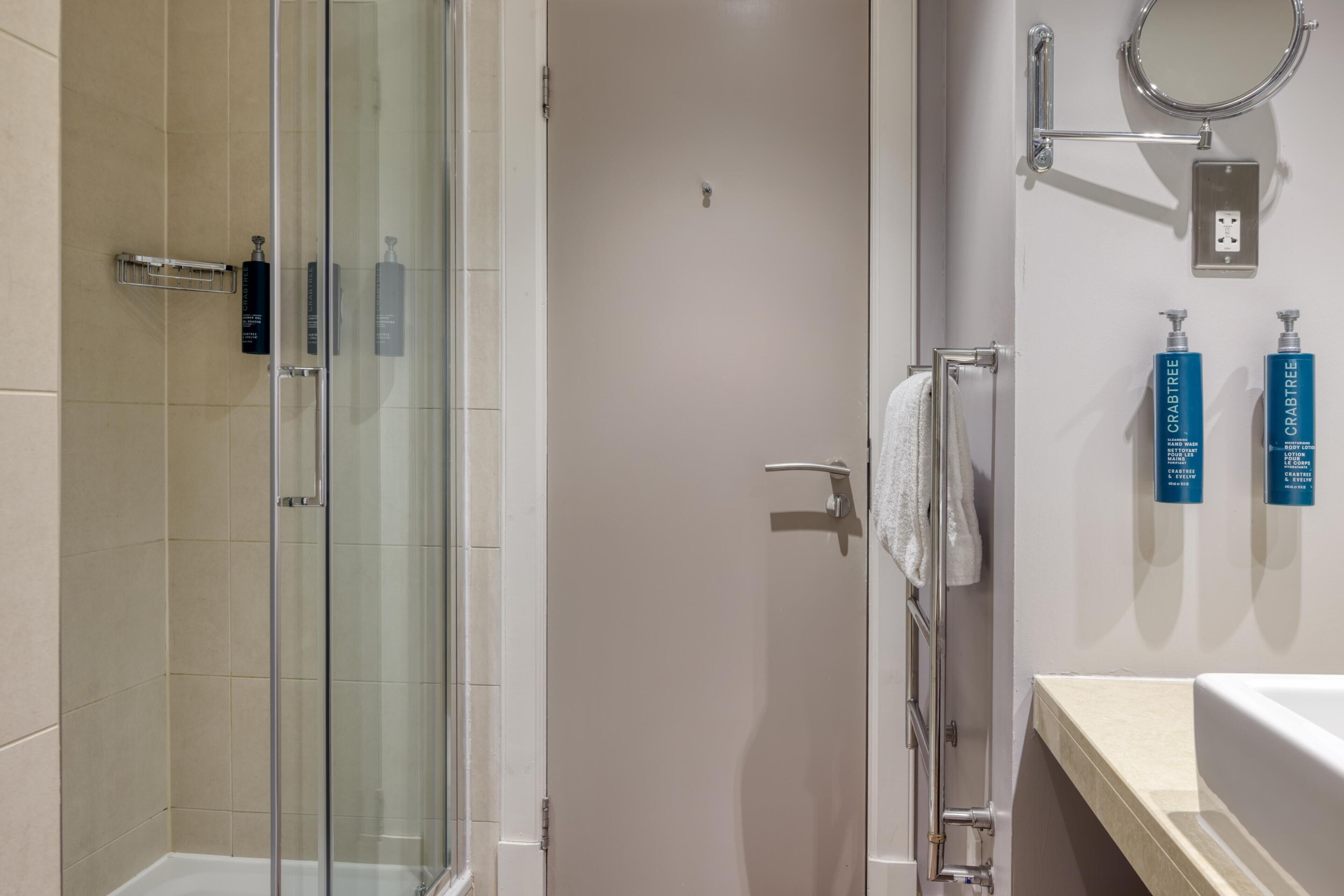 Un baño moderno con cabina de ducha de vidrio, un lavamanos blanco y dos botellas de champú Crabtree en la pared.