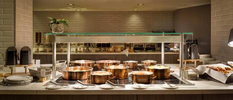 A buffet setup with multiple copper pots, a glass-top serving station, and a potted plant.