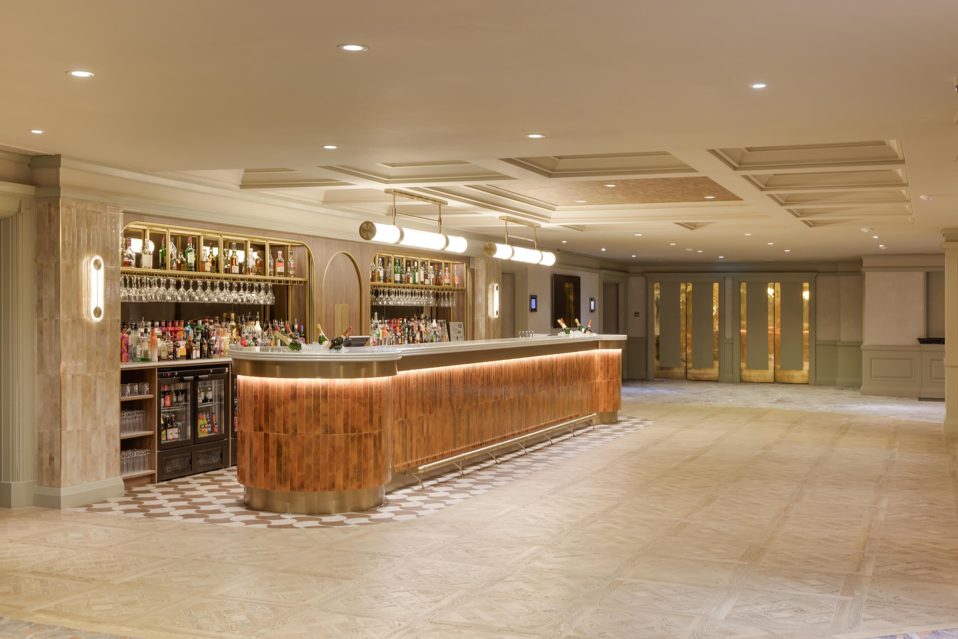 A bar area with a wooden counter, shelves with bottles, and glasses.