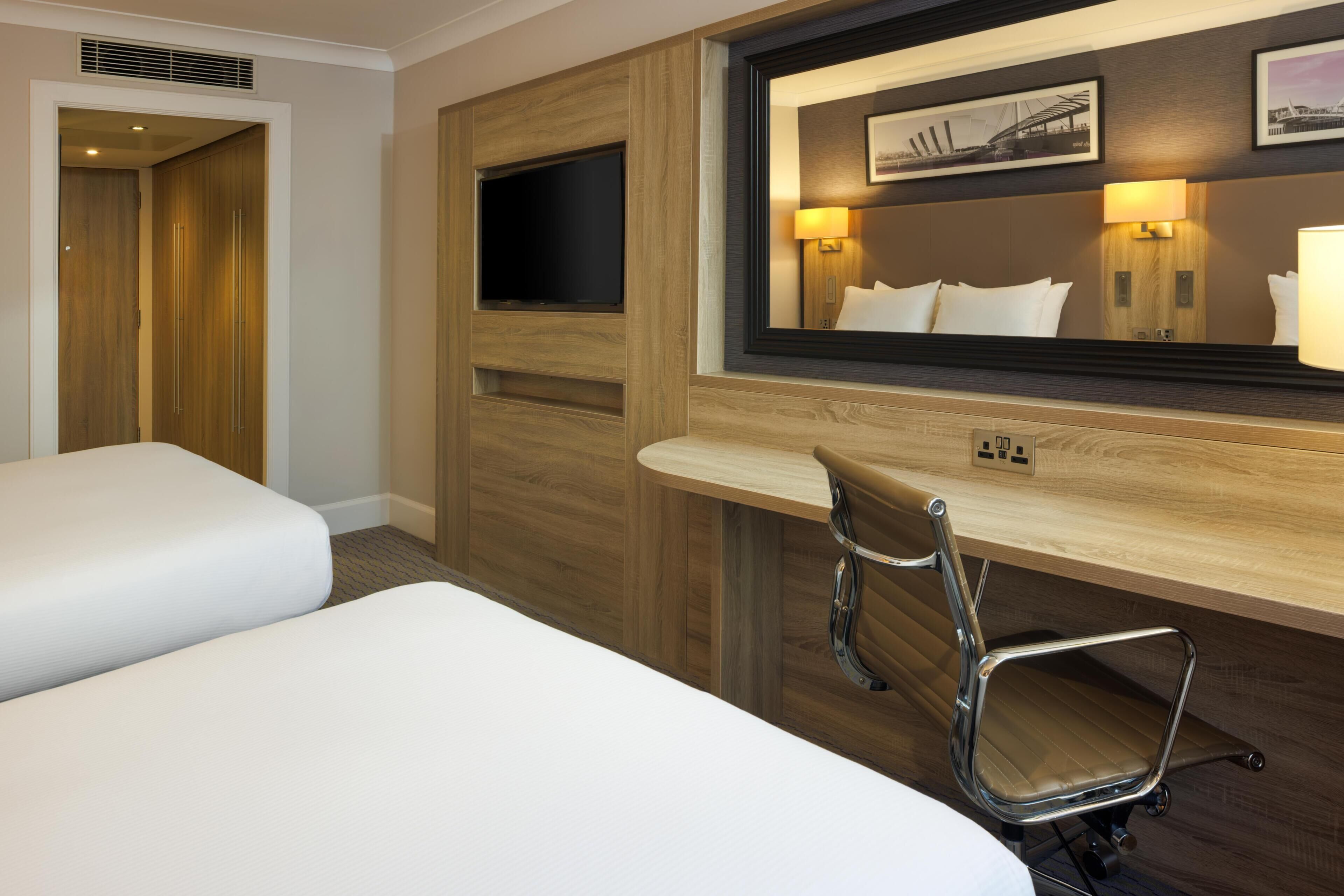 Une chambre d’hôtel avec un lit, un bureau, une chaise, une télévision et un miroir.