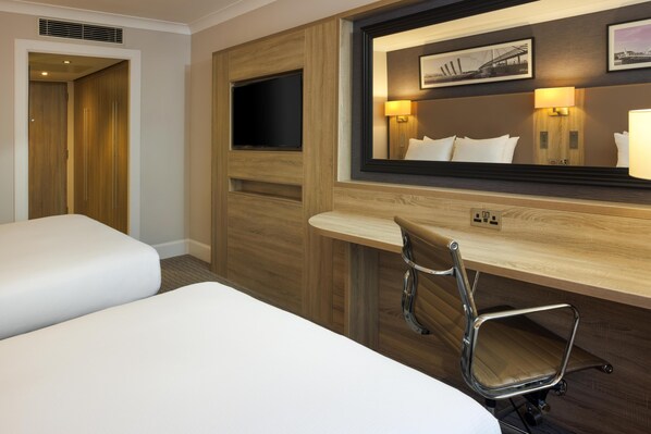 Habitación de hotel con cama, escritorio, silla, televisor y espejo.