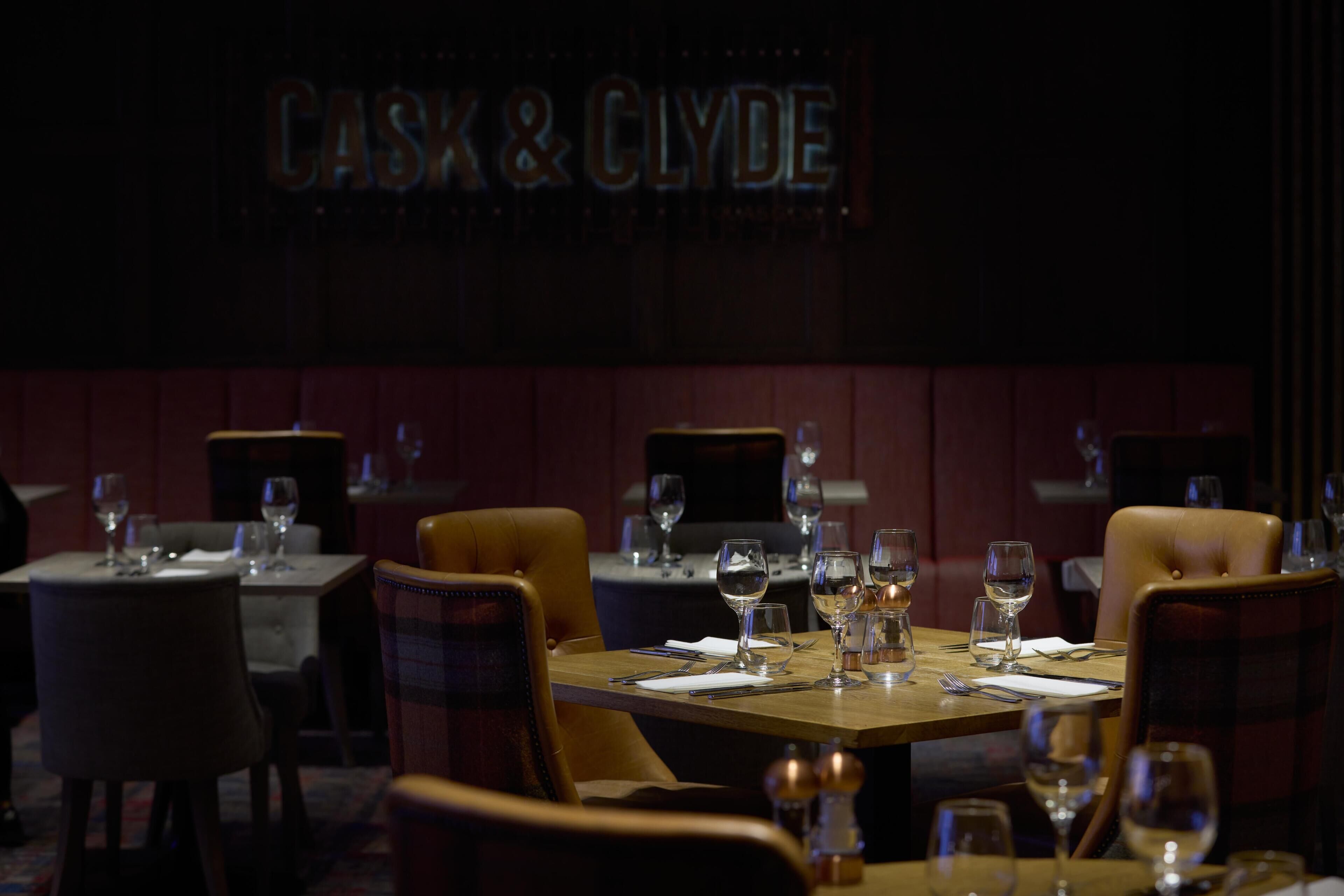 A restaurant interior with tables set for dining, a sign reading 'CASK & CLYDE,' and a dark, moody ambiance.