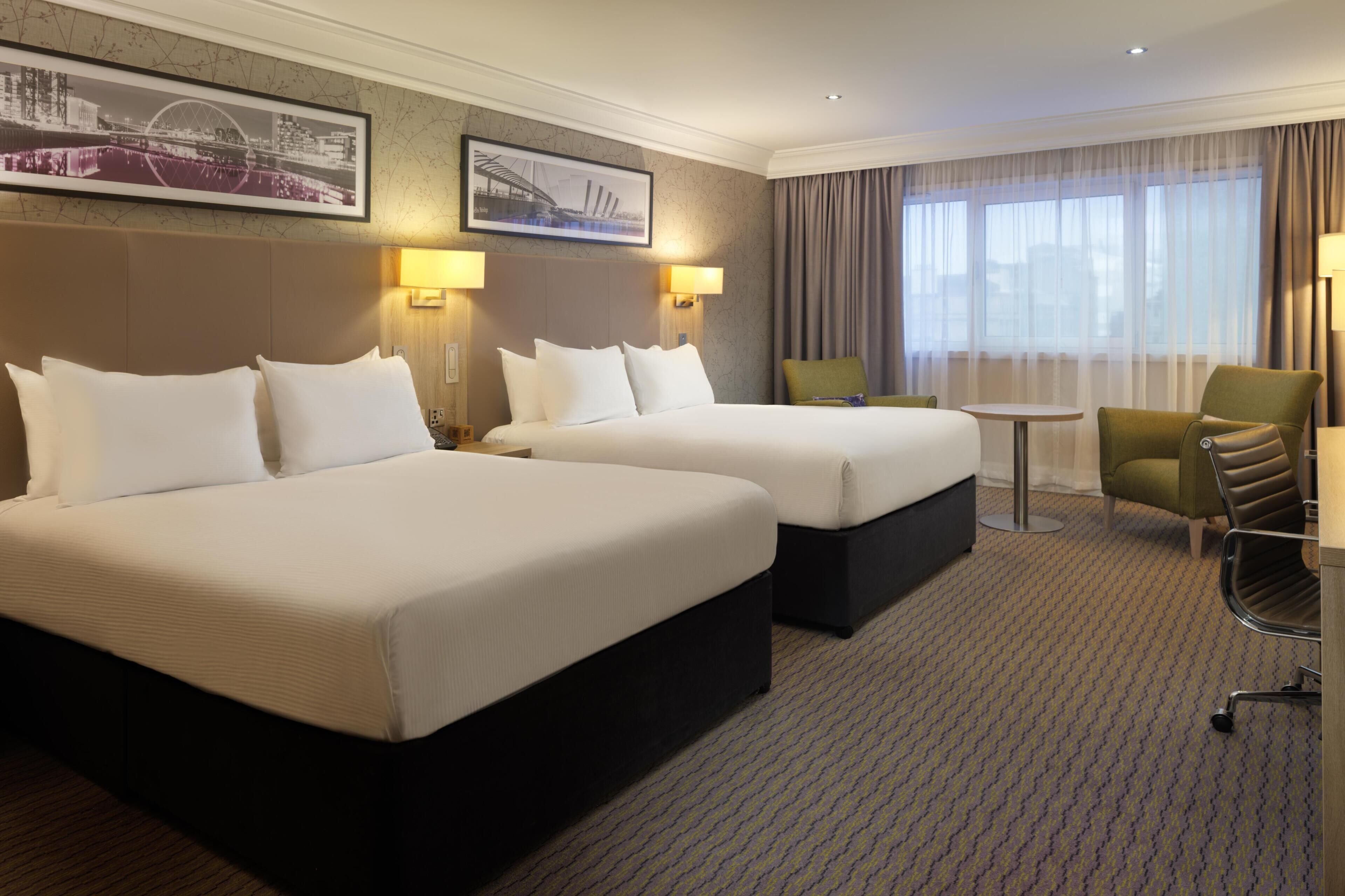 A hotel room with two beds, a small table, a chair, and two lamps.
