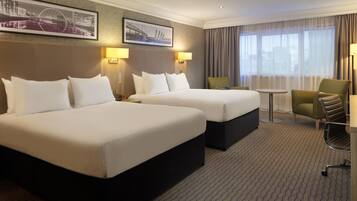 A hotel room with two beds, a small table, a chair, and two lamps.