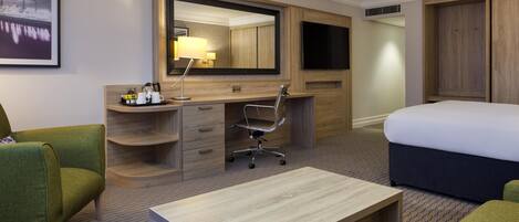 A hotel room with a bed, a desk, a chair, a large mirror, a TV, and a wardrobe.