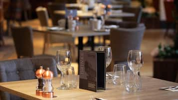 Una mesa de restaurante con un menú, saleros, pimenteros y copas de vino.