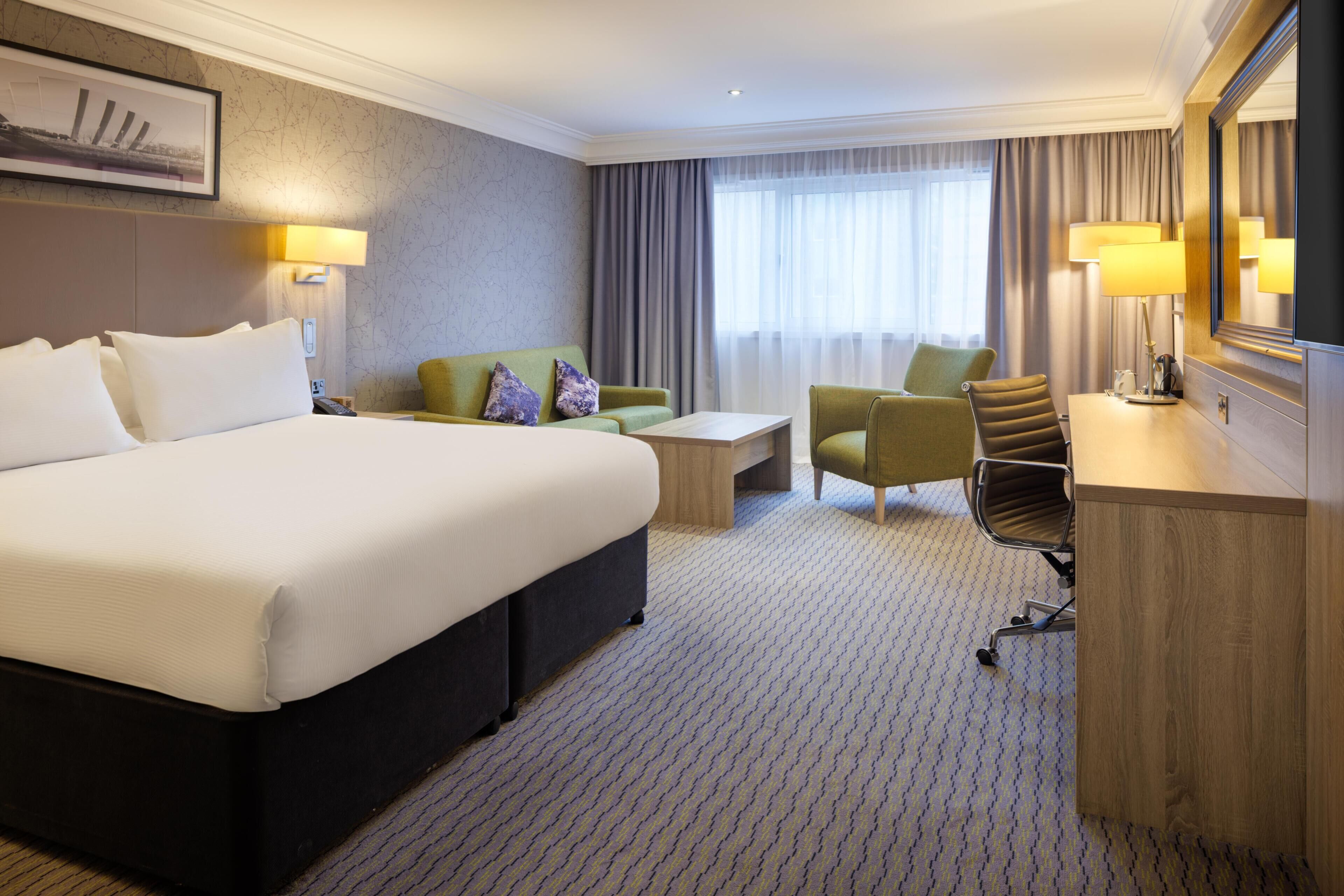 A hotel room with a large bed, a sofa, a desk, and a chair.