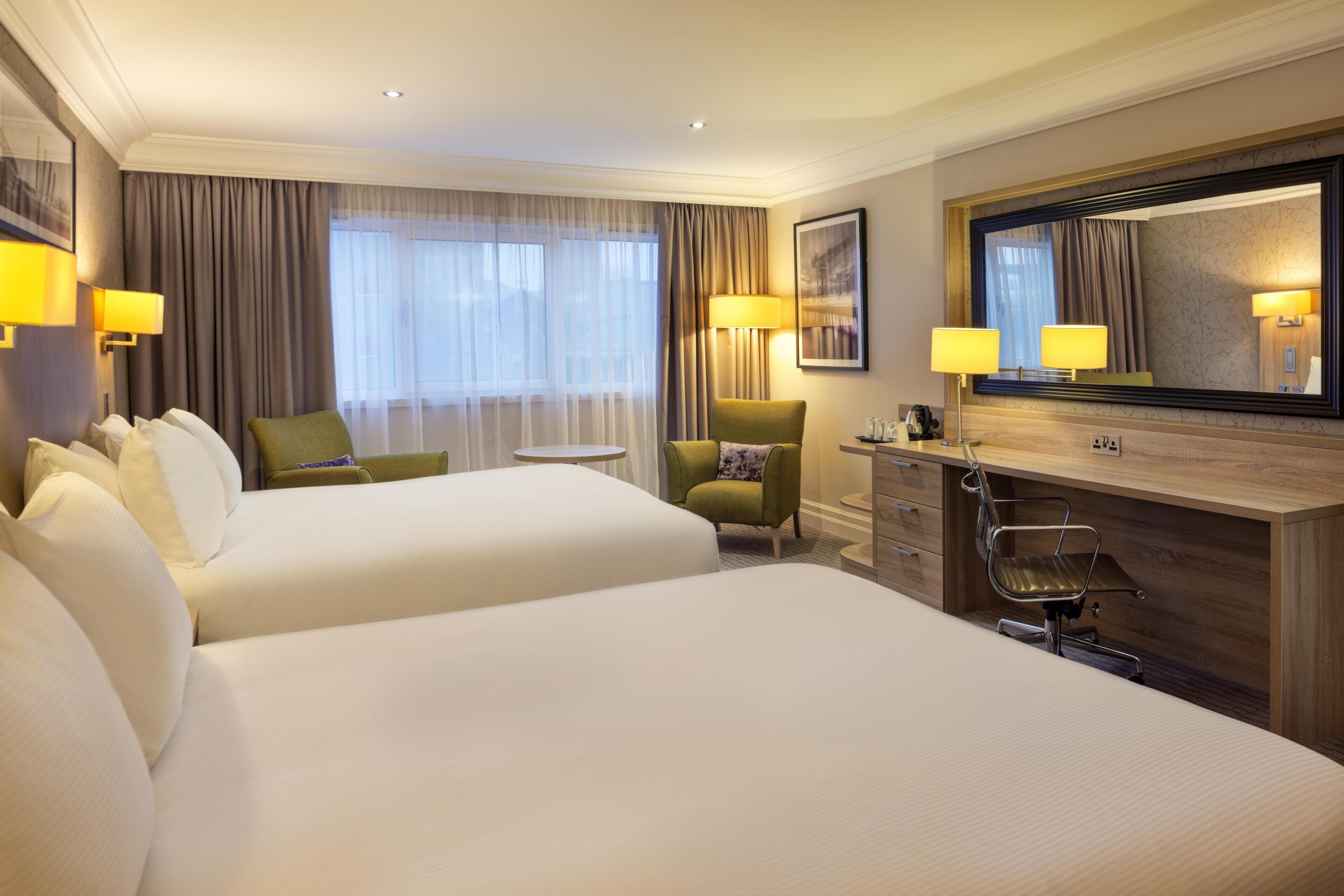 Ein Hotelzimmer mit zwei Betten, einem Schreibtisch, einem Stuhl, einem Schminktisch und einem großen Spiegel.