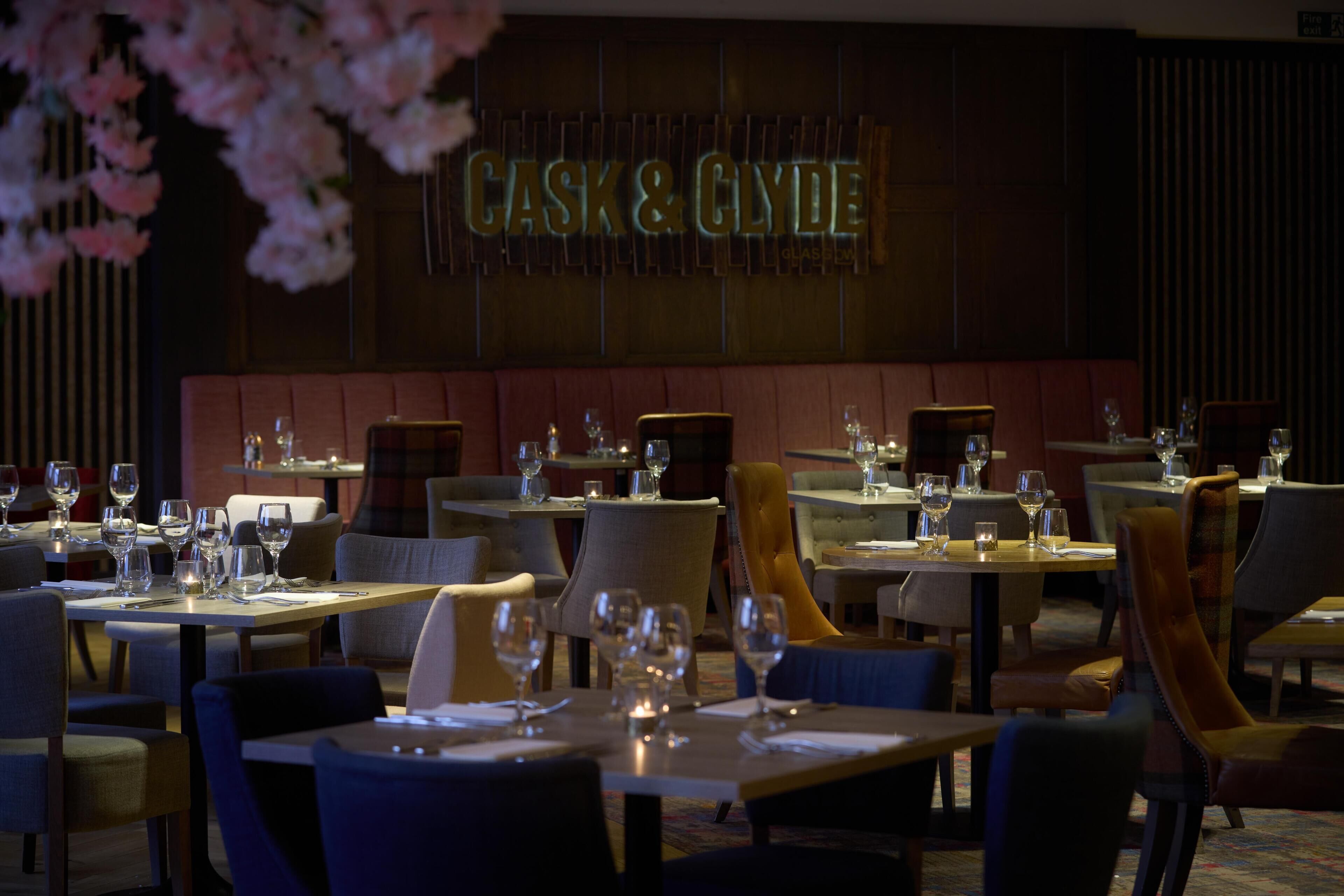 Un restaurante con mesas dispuestas para comer, un letrero que dice 'CASK & CLYDE' y un interior oscuro.