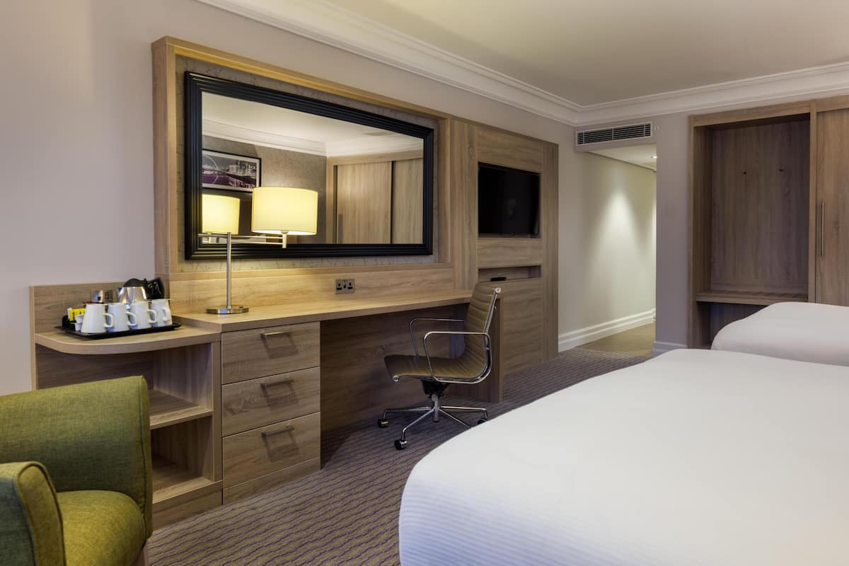 Een hotelkamer met een groot bed, een bureau met stoel, een dressoir, een spiegel en een televisie.