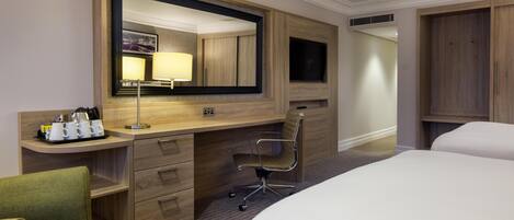 A hotel room with a large bed, a desk with a chair, a dresser, a mirror, and a television.