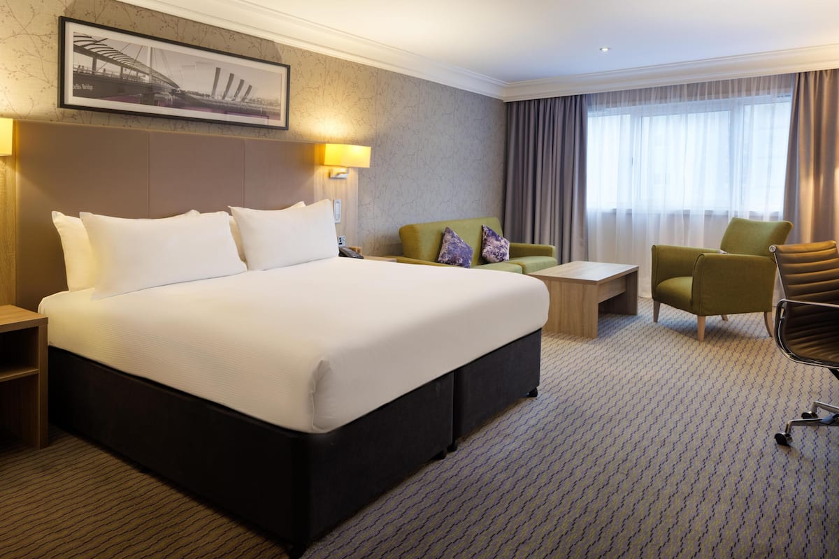 Een hotelkamer met een groot bed, een groene fauteuil, een tafeltje en een stoel.