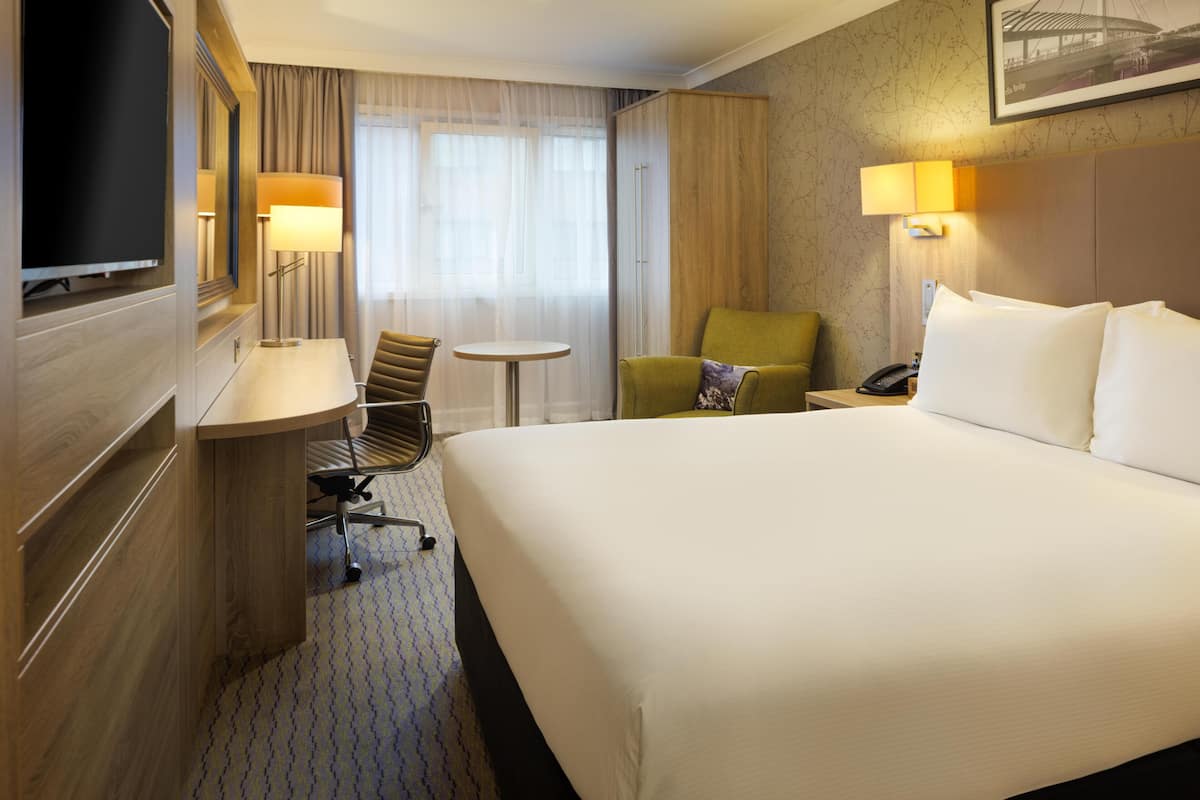 Een hotelkamer met een groot bed, een bureau met stoel, een bijzettafeltje, een televisie en een lamp.