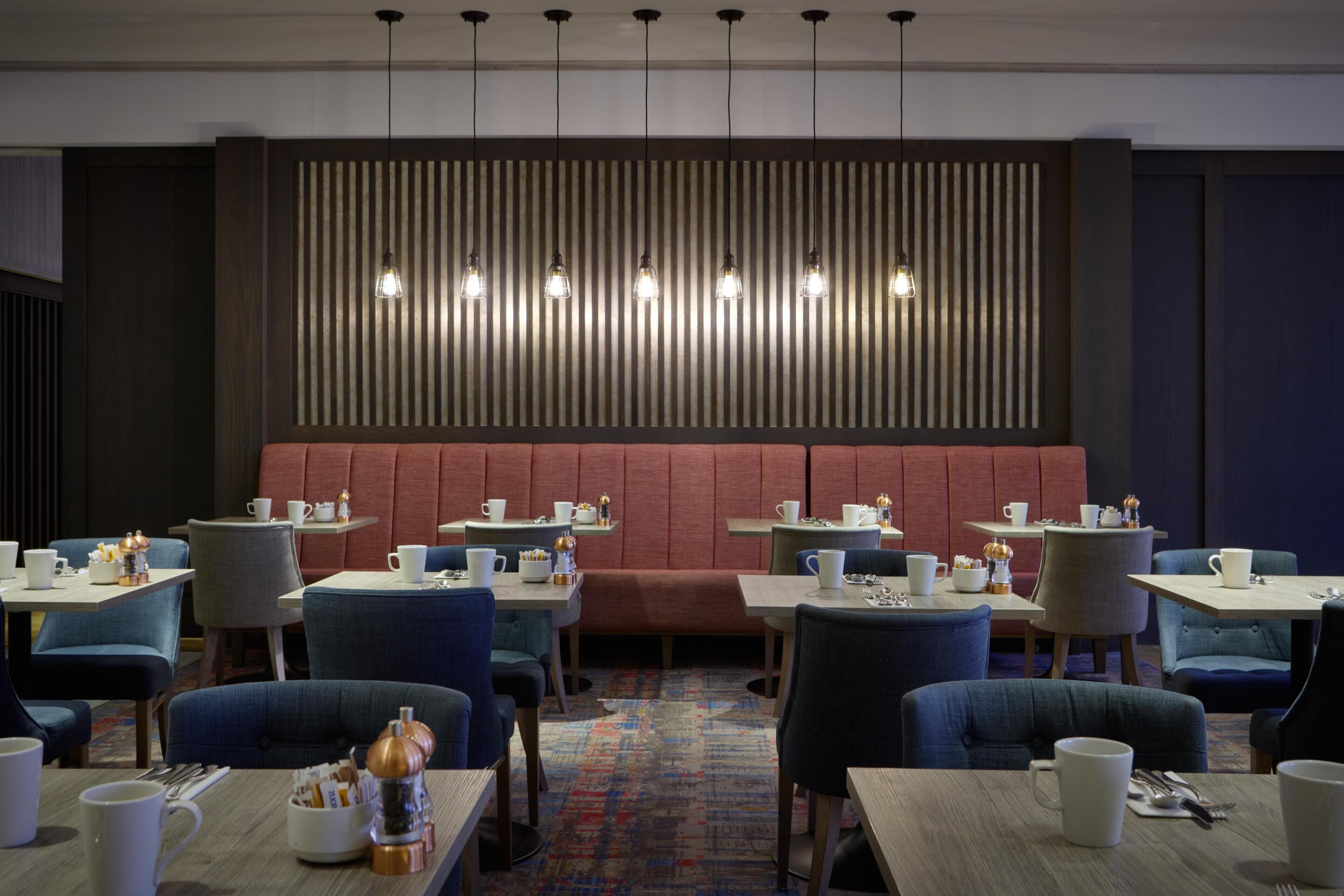 A modern dining area with booths, tables, and chairs, featuring a patterned wall and pendant lighting.