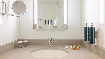 Ein modernes Badezimmer mit einem runden Spiegel, einem Waschbecken, einer Handbrause und Pflegeprodukten an der Wand.
